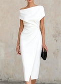 A woman wearing a white off-the-shoulder midi dress with a gathered waist and wrap-style skirt, holding a black clutch against a textured beige wall.