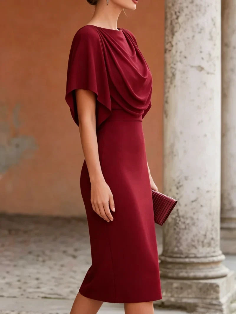 Woman wearing a burgundy dress with a draped bodice in an outdoor setting.