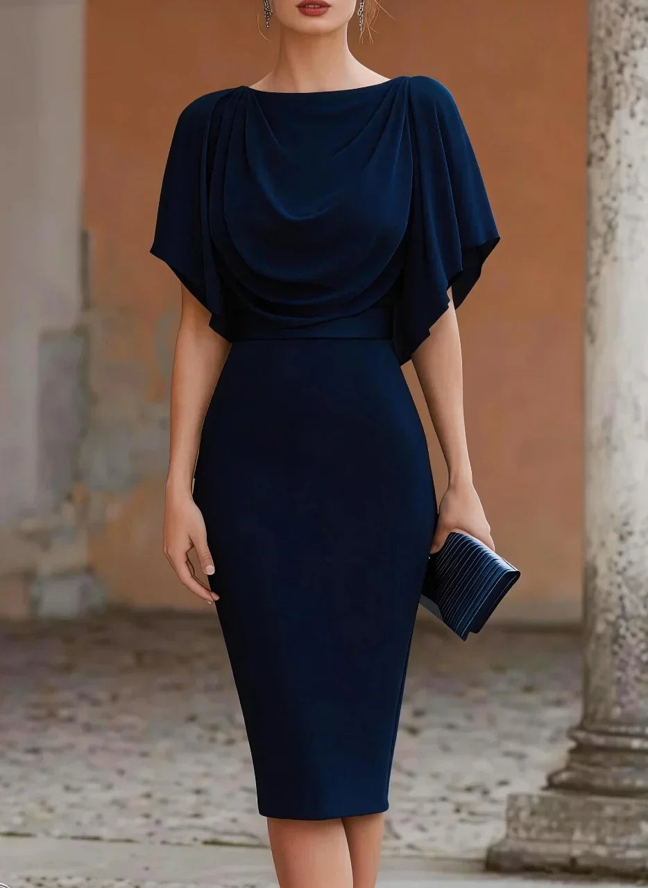 Woman wearing a navy blue dress with a draped neckline in an outdoor setting.